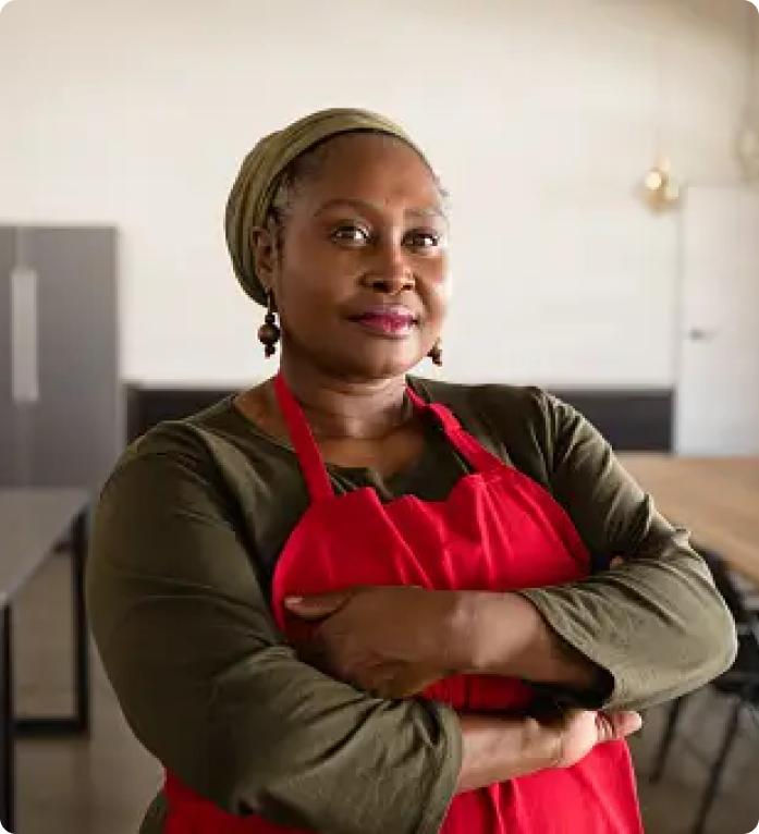 Picture of a black adult woman with a red apron on, her hands are folded around her chest