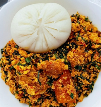 A plate of Semovita and Egusi soup, some meats can be seen above the soup.