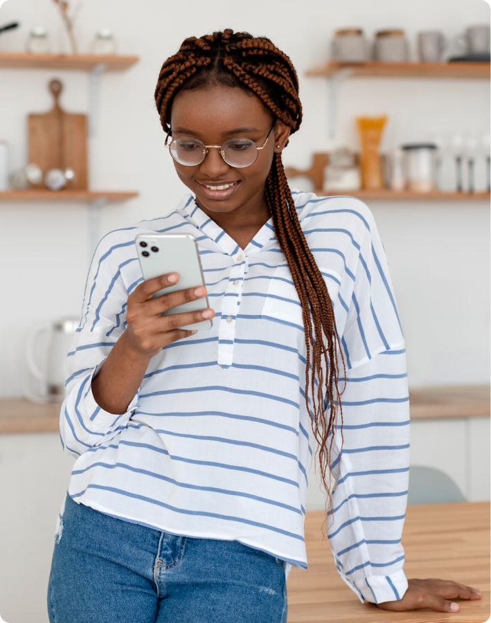 A picture of a lady standing with her phone and her other hand on the table, she's looking into her phone with her lips slightly parted