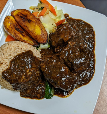 A carefully molded rice is overlayed with some African local soup, beside it are some fried plantains and vegetables.